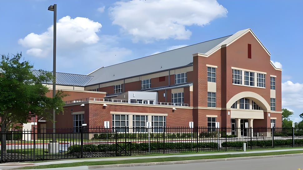 Das mehrstöckige Backsteingebäude der The Village School mit einem gewölbten Eingang steht in einer Grünfläche.