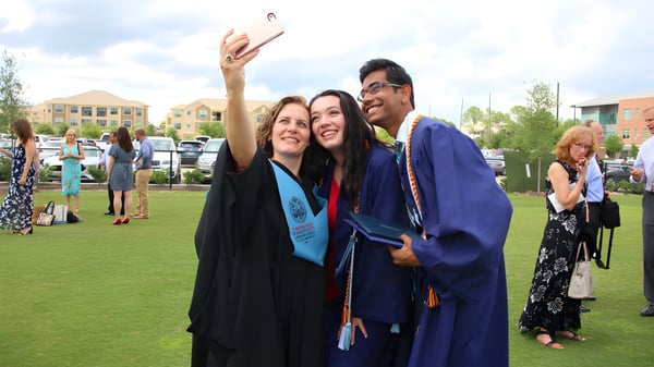 Drei Absolventen der The Village School machen ein Selfie auf dem Campus mit Gebäuden im Hintergrund.