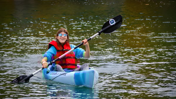 Eine Person in roter Schwimmweste paddelt mit einem blauen Kajak auf dem Wasser auf dem Gelände der The Village School.