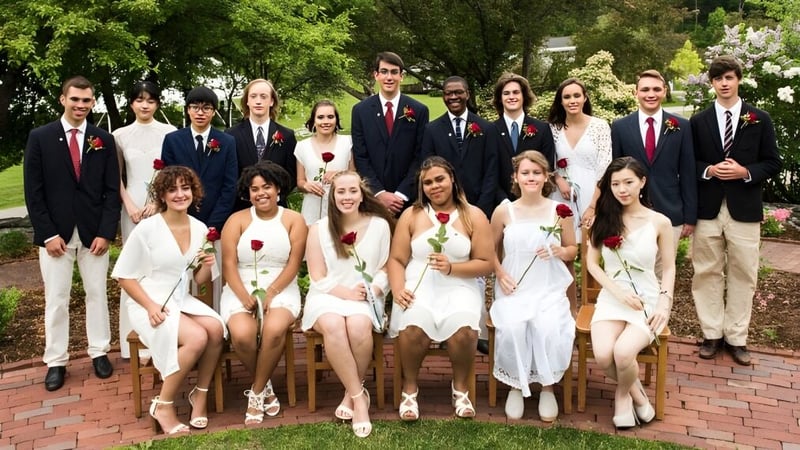 Eine Gruppe Schüler der The White Mountain School posiert gemeinsam formell gekleidet in einem Gartenbereich mit grüner Vegetation und Backsteinmauern.
