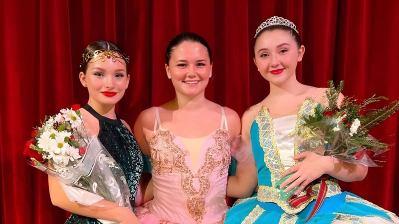 Drei Frauen in aufwendigen Kostümen und Kronen stehen mit Blumensträußen vor dem roten Vorhang auf einer Veranstaltung der The White Mountain School.