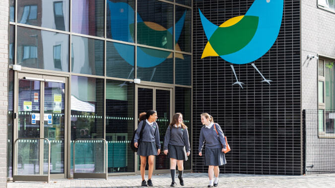Drei Personen in Businesskleidung stehen vor einem Gebäude mit einem großen abstrakten Wandbild auf dem Campus der The Wren School.