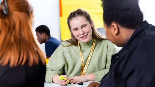 Eine Frau im grünen Pullover führt ein Gespräch mit zwei Personen auf dem Campus der The Wren School.