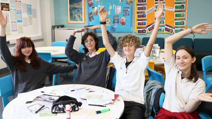 Eine Gruppe Schüler der The Wren School meldet sich im Klassenraum mit bunten Lernplakaten an den Wänden.