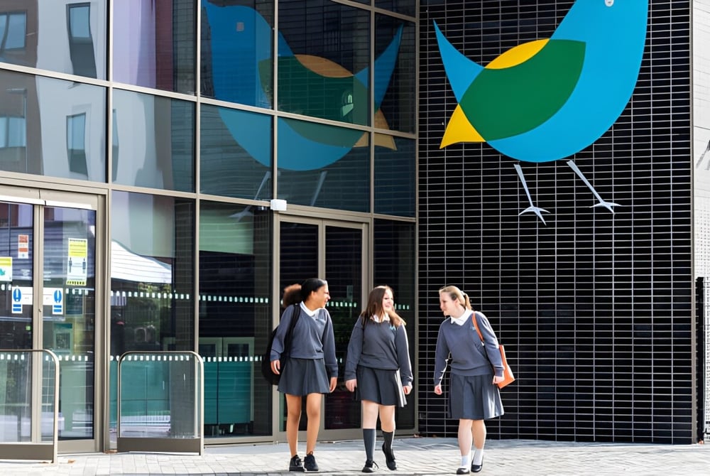 Drei Schüler stehen vor einem Gebäude mit großen Fenstern und einem farbenfrohen Wandbild an der The Wren School.