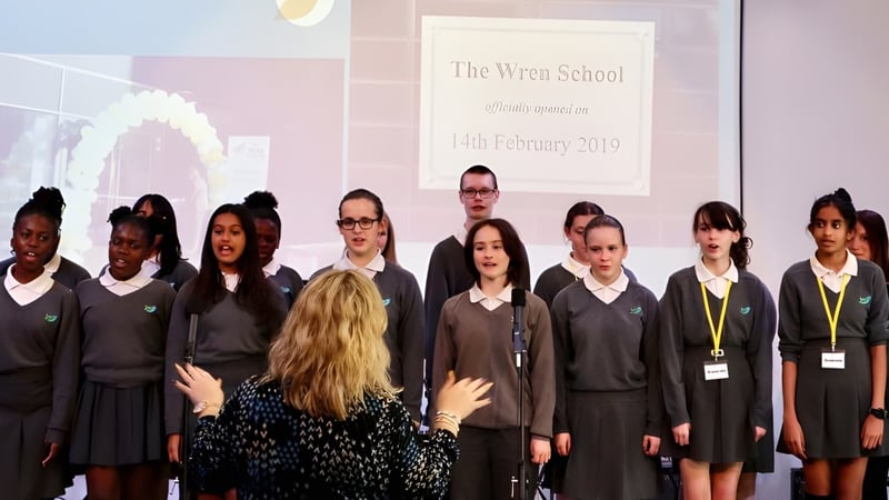 Schüler der The Wren School stehen vor einer Leinwand, auf der der Schulname und das Datum 6. Februar 2019 angezeigt werden.