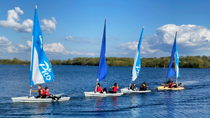 Schüler der Theale Green School segeln mit kleinen Segelbooten auf einem ruhigen See.