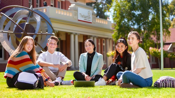 Eine Gruppe Schülerinnen und Schüler sitzt auf dem Gras vor einem Backsteingebäude auf dem Campus des Thebarton Senior College.