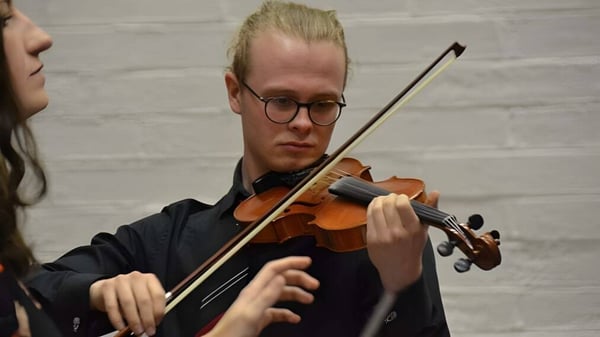 Ein Schüler der The High School spielt konzentriert Geige vor einer weißen Backsteinwand.