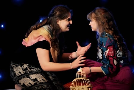 Zwei Schülerinnen der Thetford Grammar School umarmen sich vor dunklem Hintergrund mit funkelnden Lichtern.
