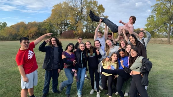 Eine Gruppe von Schülerinnen und Schülern der Thomas A. Blakelock High School versammelt sich draußen in einem parkähnlichen Bereich mit Bäumen und Wiese.