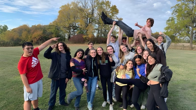 Eine Gruppe von Schülerinnen und Schülern der Thomas A. Blakelock High School versammelt sich draußen in einem parkähnlichen Bereich mit Bäumen und Wiese.