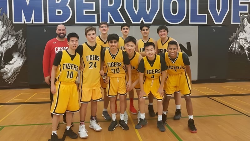 Eine Gruppe junger Basketballspielerinnen und -spieler der Thornhill Secondary School posiert vor einem Timberwolves-Banner auf dem Basketballfeld.