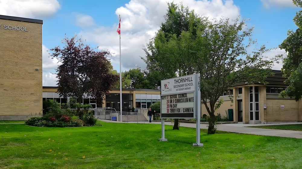 Das Schulgebäude der Thornhill Secondary School ist von Bäumen umgeben und im Vordergrund befindet sich eine Rasenfläche mit einer kanadischen Flagge.