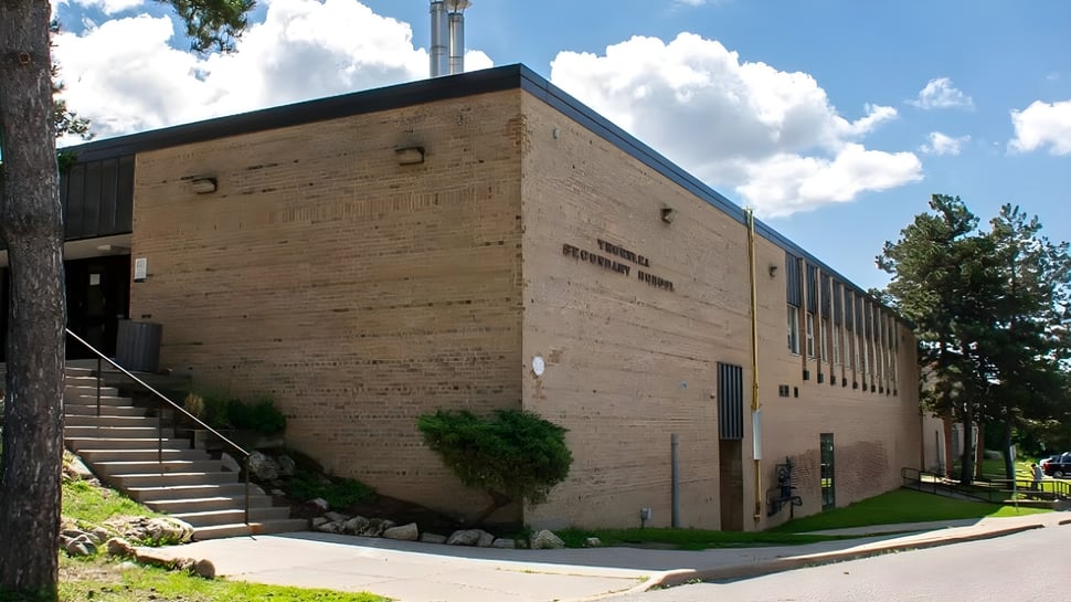 Das große Backsteingebäude der Thornlea Secondary School mit Treppen und Bäumen davor unter bewölktem Himmel.