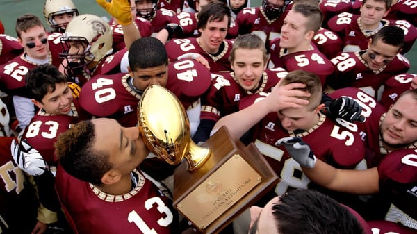Eine Gruppe von Fußballspielern feiert den Gewinn einer Trophäe auf dem Gelände der Thornton Academy.