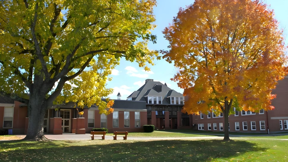 Historisches Gebäude der Thornton Academy im herbstlichen Park mit bunten Bäumen und Bänken auf der Wiese.