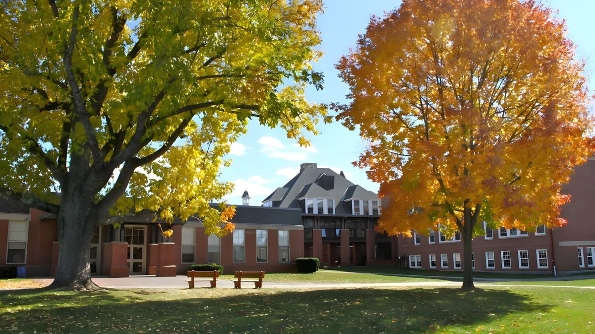 Historisches Gebäude der Thornton Academy im herbstlichen Park mit bunten Bäumen und Bänken auf der Wiese.