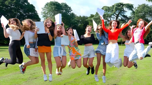 Eine Gruppe junger Schülerinnen des Thornton College feiert gemeinsam und springt auf einer grasbewachsenen Fläche im Freien.