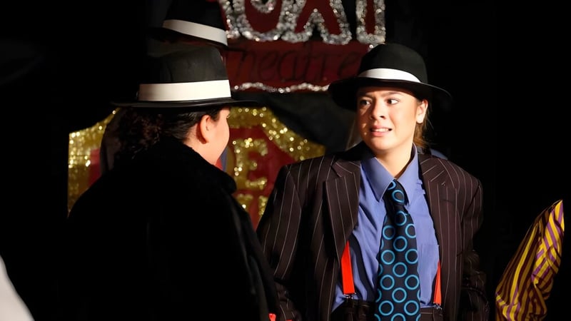 Zwei Schülerinnen des Thornton College tragen stilvolle Hüte und Anzüge vor einem farbenfrohen gemusterten Hintergrund.