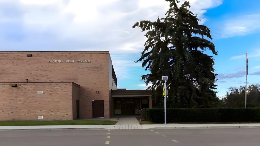 Das Backsteingebäude der Thorsby Junior Senior High School mit großem Eingang und einem hohen Nadelbaum im Vordergrund.