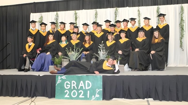 Absolventen der Thorsby Junior Senior High School posieren im Abschlussgewand vor einem Banner mit der Aufschrift Grad 2021.