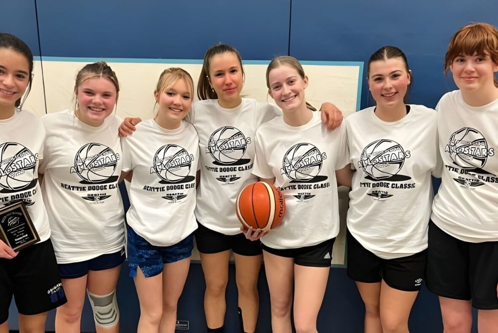 Eine Gruppe Schülerinnen der Thousand Islands Secondary School trägt weiße T-Shirts mit Basketballlogo und posiert gemeinsam in einer Sporthalle.