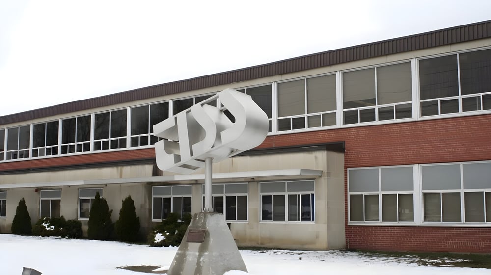 Das moderne Gebäude der Thousand Islands Secondary School mit einer Skulptur im Vordergrund und schneebedeckten Bäumen im Winter.