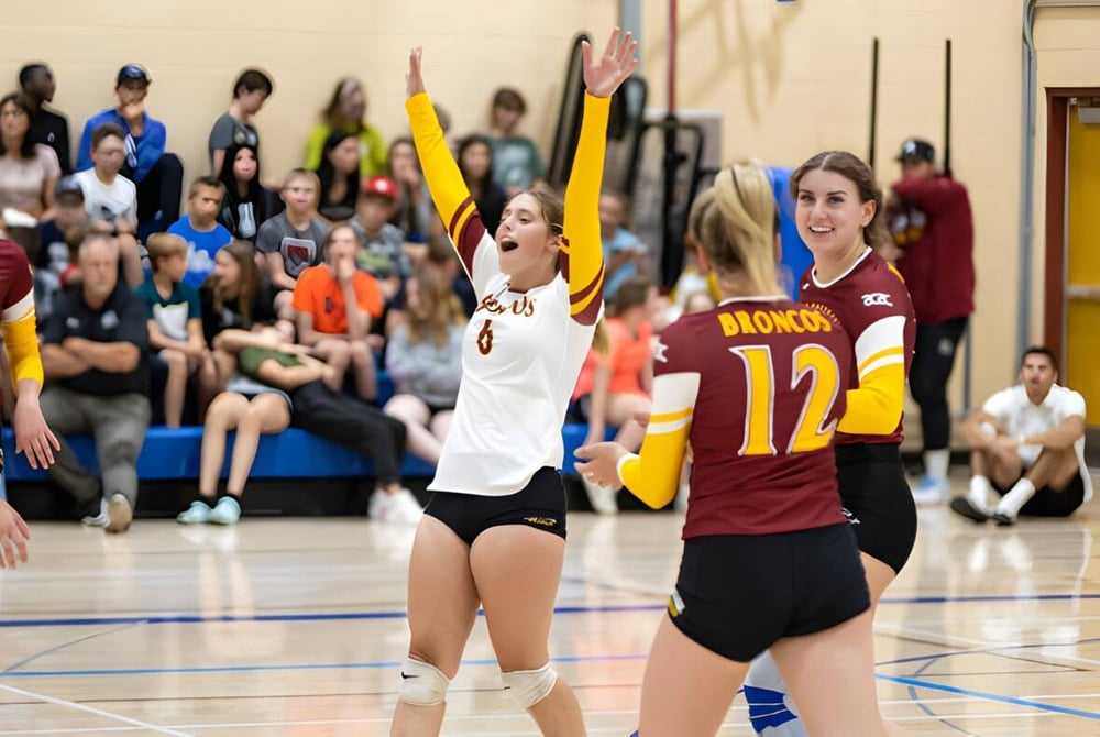 Schülerinnen der Three Hills School spielen Volleyball auf dem Außenplatz mit Zuschauern im Hintergrund.