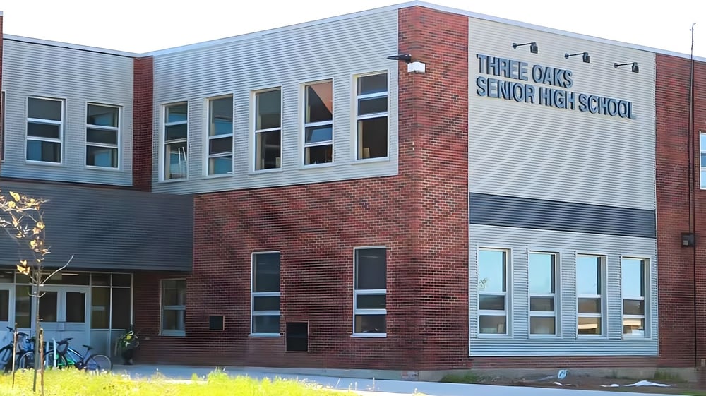 Das moderne Gebäude der Three Oaks Senior High School mit Backstein- und Glasfassade ist von gepflegter Bepflanzung umgeben.