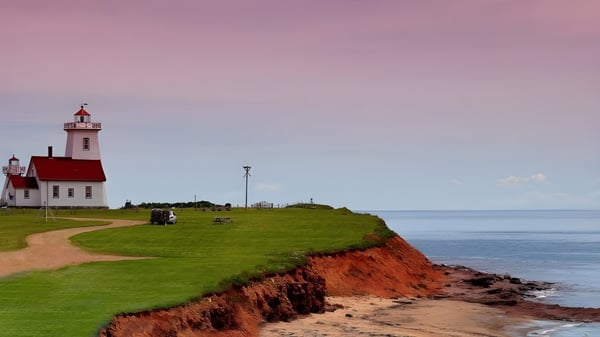 Ein Leuchtturm steht auf einem grasbewachsenen Hügel mit Blick auf die Felsküste und das Meer auf dem Gelände der Three Oaks Senior High.