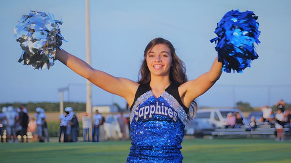Eine Cheerleaderin der Thunder Ridge High School steht auf dem Sportfeld und winkt mit blauen und silbernen Pompons.