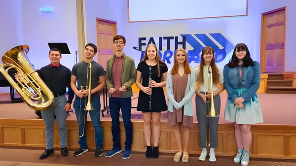 Eine Gruppe von Schülern der Thunder Ridge High School steht mit Musikinstrumenten vor einem großen Faith-Banner in einem Kirchenraum.