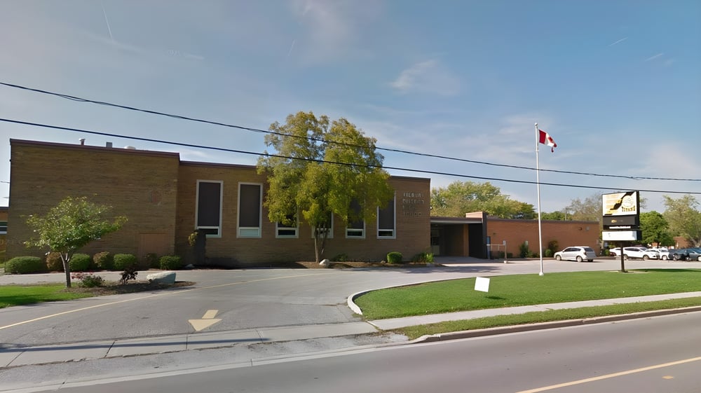 Das Backsteingebäude der Tilbury District High School mit einer kanadischen Flagge auf einem Fahnenmast und Bäumen drumherum.
