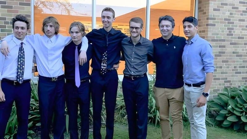 Eine Gruppe Schüler steht vor einem Backsteingebäude mit einer orangefarbenen Wand auf dem Campus der Tilbury District High School.