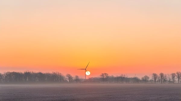 Windturbine vor einem farbenfrohen Sonnenuntergang über einem nebligen Feld in der Umgebung der Tilbury District High School.