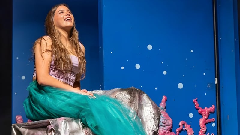 Eine junge Frau sitzt auf einer Bühne vor einem blauen Hintergrund mit weißen Punkten auf dem Campus der Tilton School.