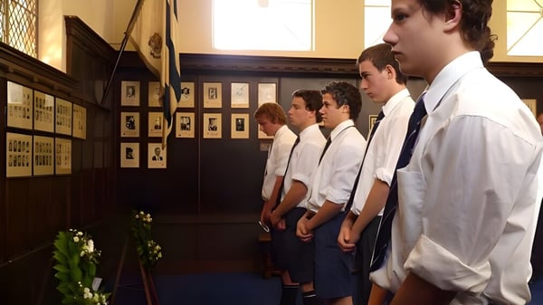 Schüler der Timaru Boys School stehen vor einer Wand mit gerahmten Fotografien und einer Blumenarrangement.