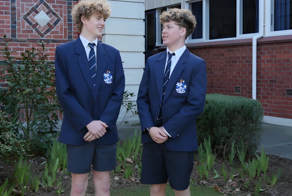 Zwei Schüler der Timaru Boys School stehen vor einem Backsteingebäude mit diamantförmigen Fenstern.