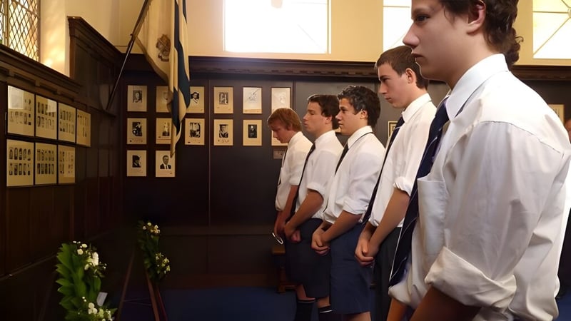 Schüler der Timaru Boys School stehen in einer Reihe vor einer Wand mit gerahmten Fotografien und einem Blumenarrangement.