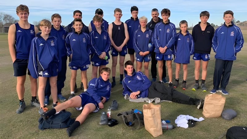 Eine Gruppe junger Athleten in blauen Uniformen steht und sitzt auf dem Sportplatz der Timaru Boys School.