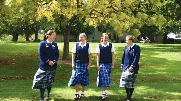 Vier Schülerinnen der Timaru Girls School stehen auf einer Wiese in einem Park mit Bäumen im Hintergrund.
