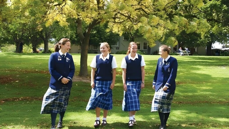 Vier Schülerinnen der Timaru Girls School stehen in Schuluniformen auf einer Wiese vor Bäumen.