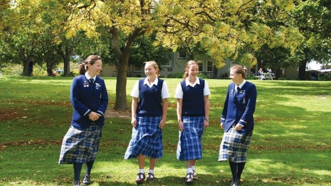 Vier Schülerinnen der Timaru Girls School stehen gemeinsam in einem Park mit Bäumen im Hintergrund.
