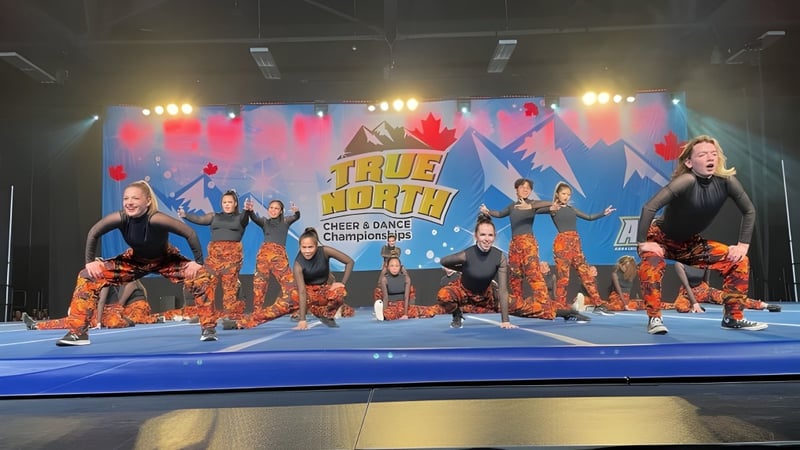 Eine Gruppe Cheerleader in bunten Uniformen führt eine Show auf der Bühne mit dem Banner der Tommy Douglas Collegiate auf.