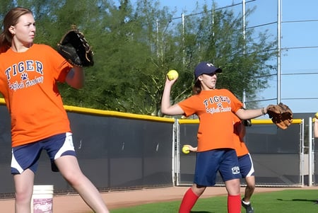 Zwei Schülerinnen in orangenen Softball-Uniformen stehen auf dem Spielfeld des Tommy Douglas Collegiate.