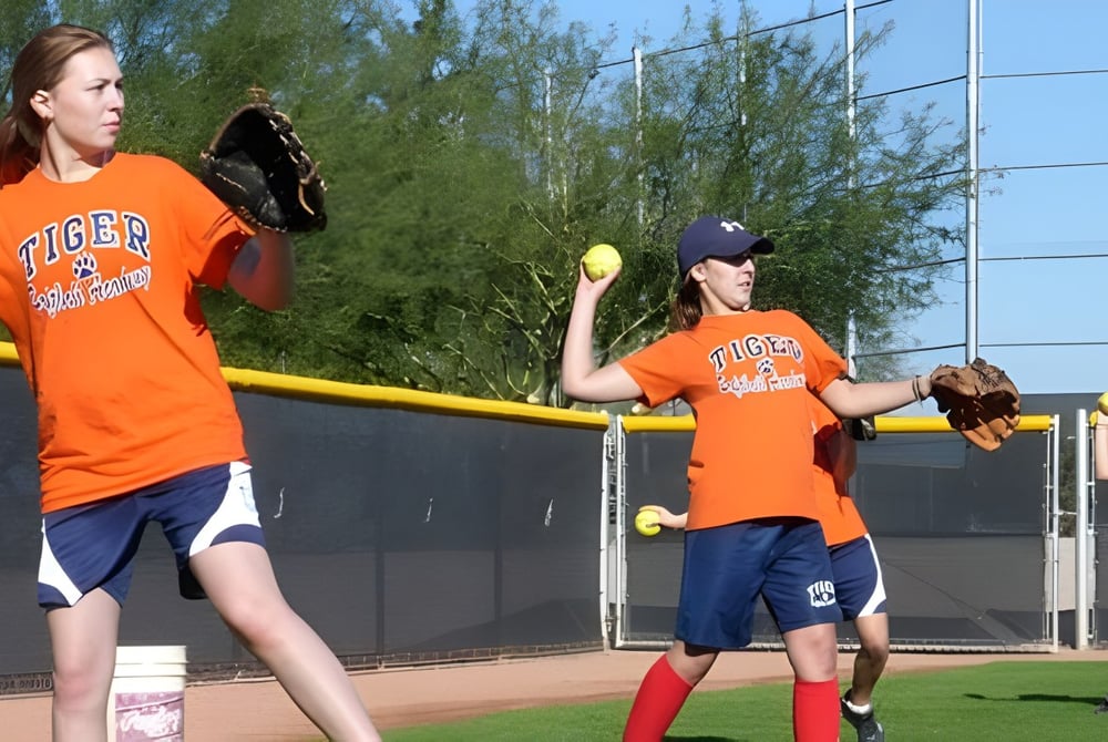 Zwei Schülerinnen in orangenen Softball-Uniformen stehen auf dem Spielfeld des Tommy Douglas Collegiate.