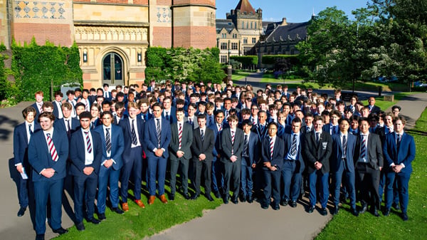 Eine große Gruppe von Schülerinnen und Schülern der Tonbridge School steht in formeller Kleidung vor einem historischen Gebäude mit reicher Architektur und umgeben von grüner Vegetation.