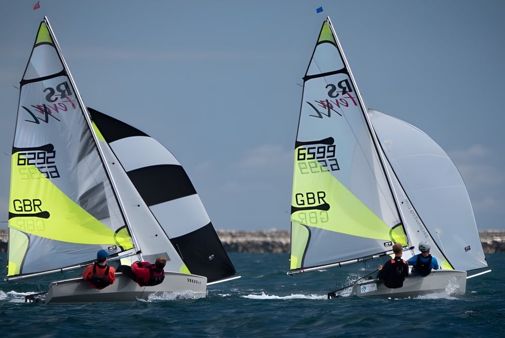 Zwei Segelboote mit britischer Flagge segeln bei blauem Himmel auf dem Wasser nahe der Tonbridge School.