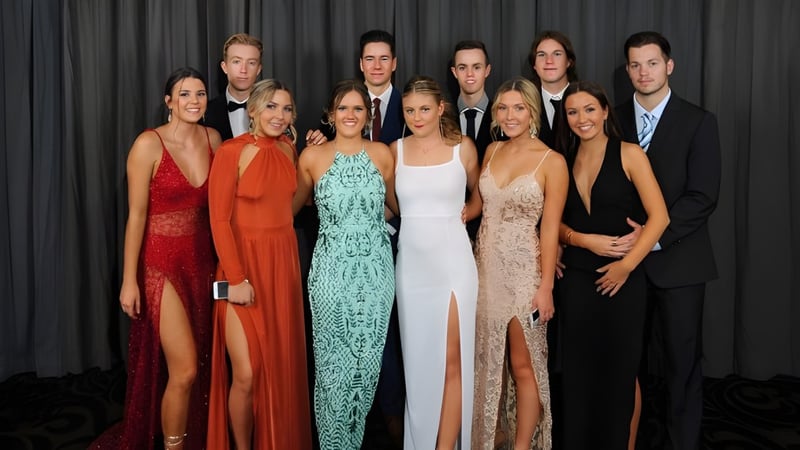 Eine Gruppe von Personen in formeller Kleidung posiert gemeinsam vor einem dunklen Hintergrund auf dem Campus der Toormina High School.